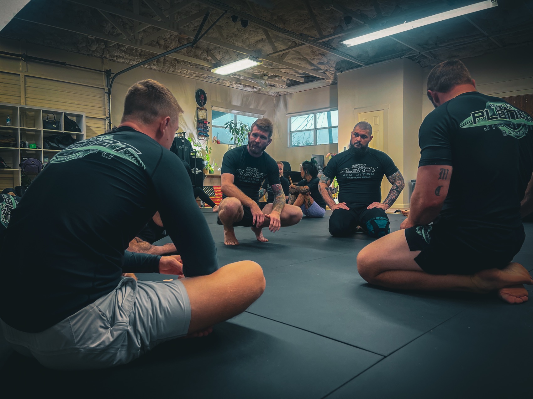 Coach Gabe Tuttle leading a no-gi jiu-jitsu mat huddle with students at 10th Planet Bastrop